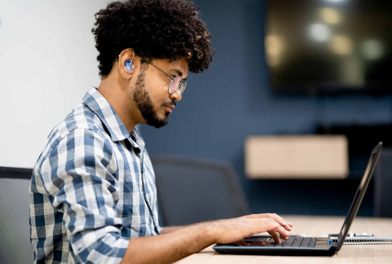 Side view of hearing impaired man working on laptop at office