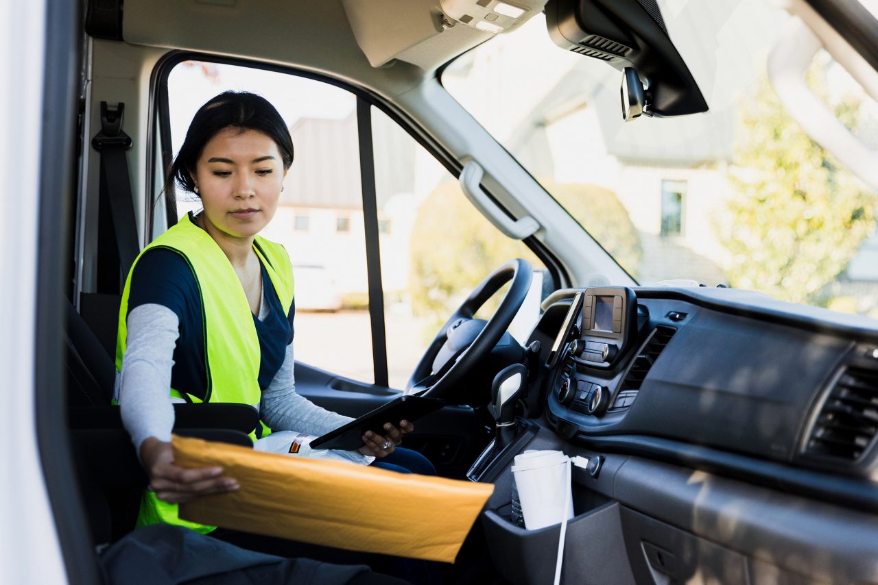 Delivery driver sits in driver's seat, checks address on envelope to be delivered