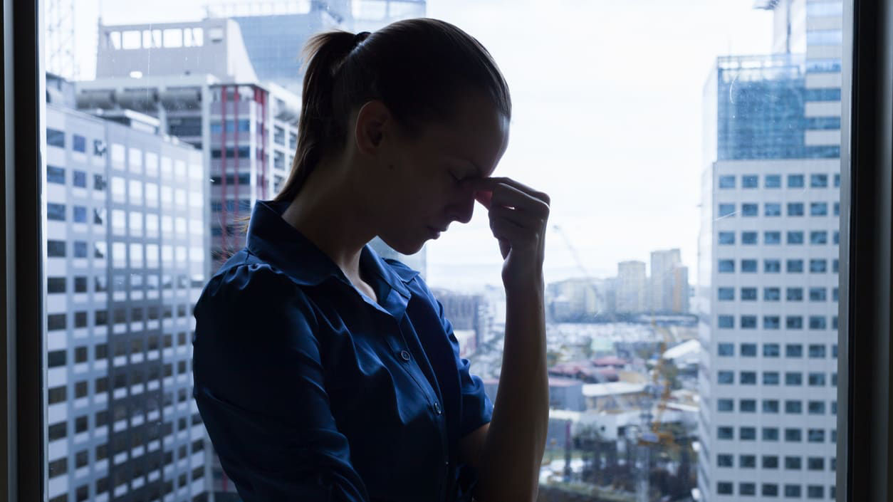 A woman is standing in front of a window with her hand on her head.
