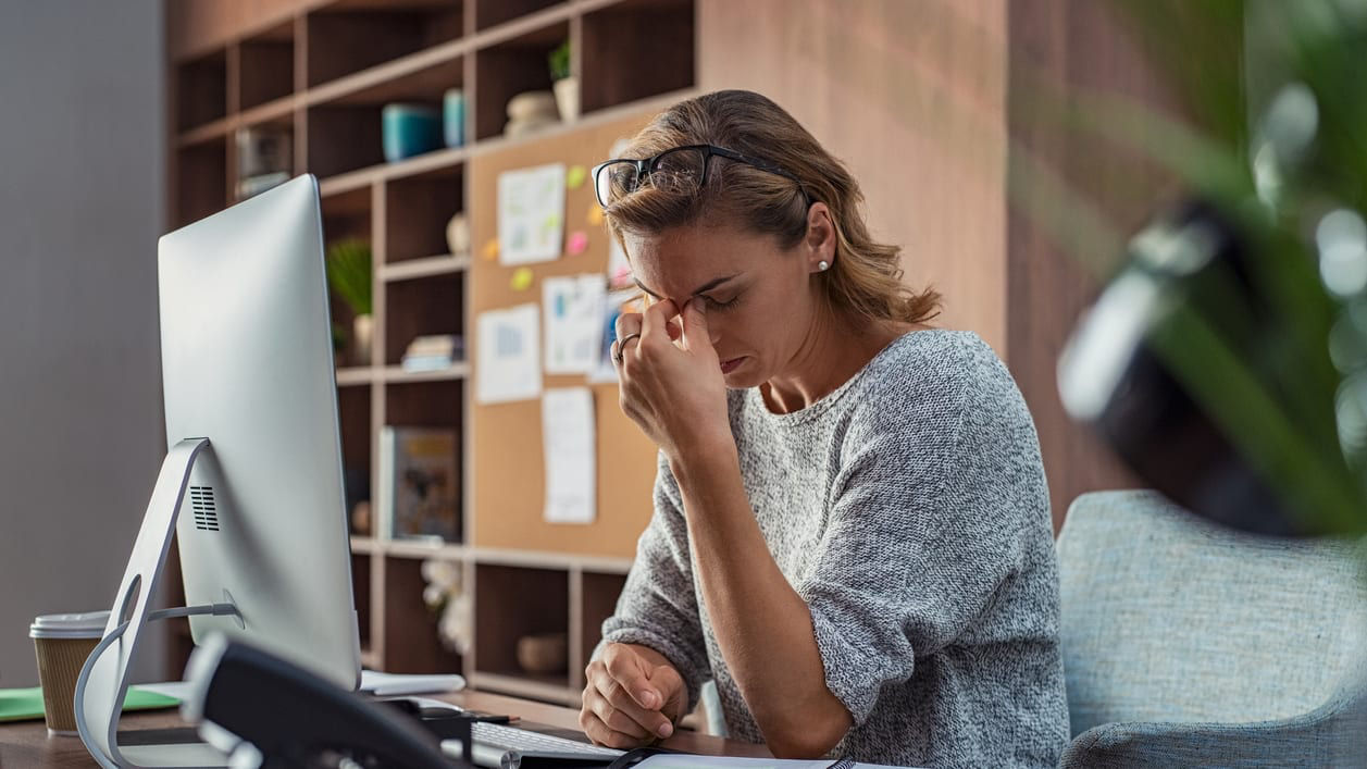 A woman is sitting at her desk with her head in her hands.