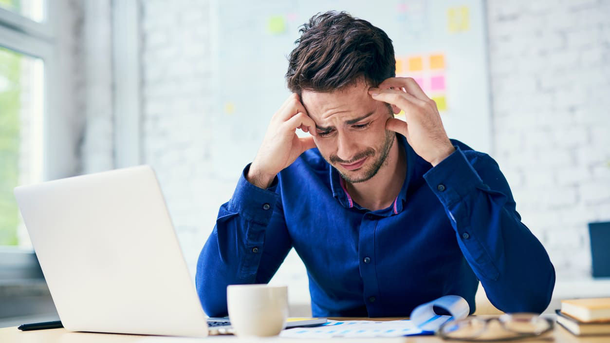 A man is sitting at his desk with his hands on his head.