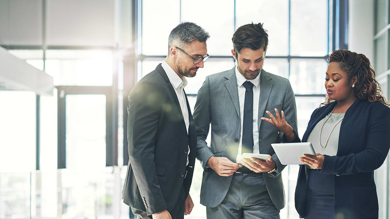 Three business people looking at a tablet in an office.