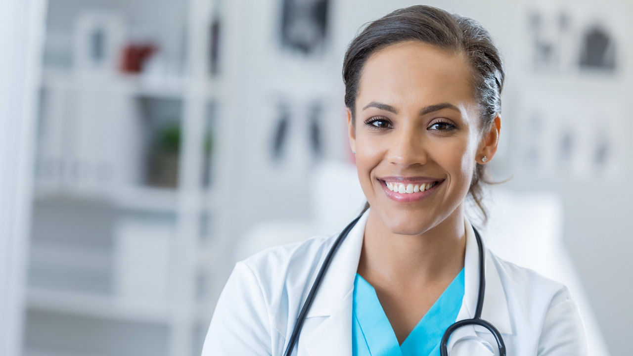 A female doctor is smiling and holding a stethoscope.