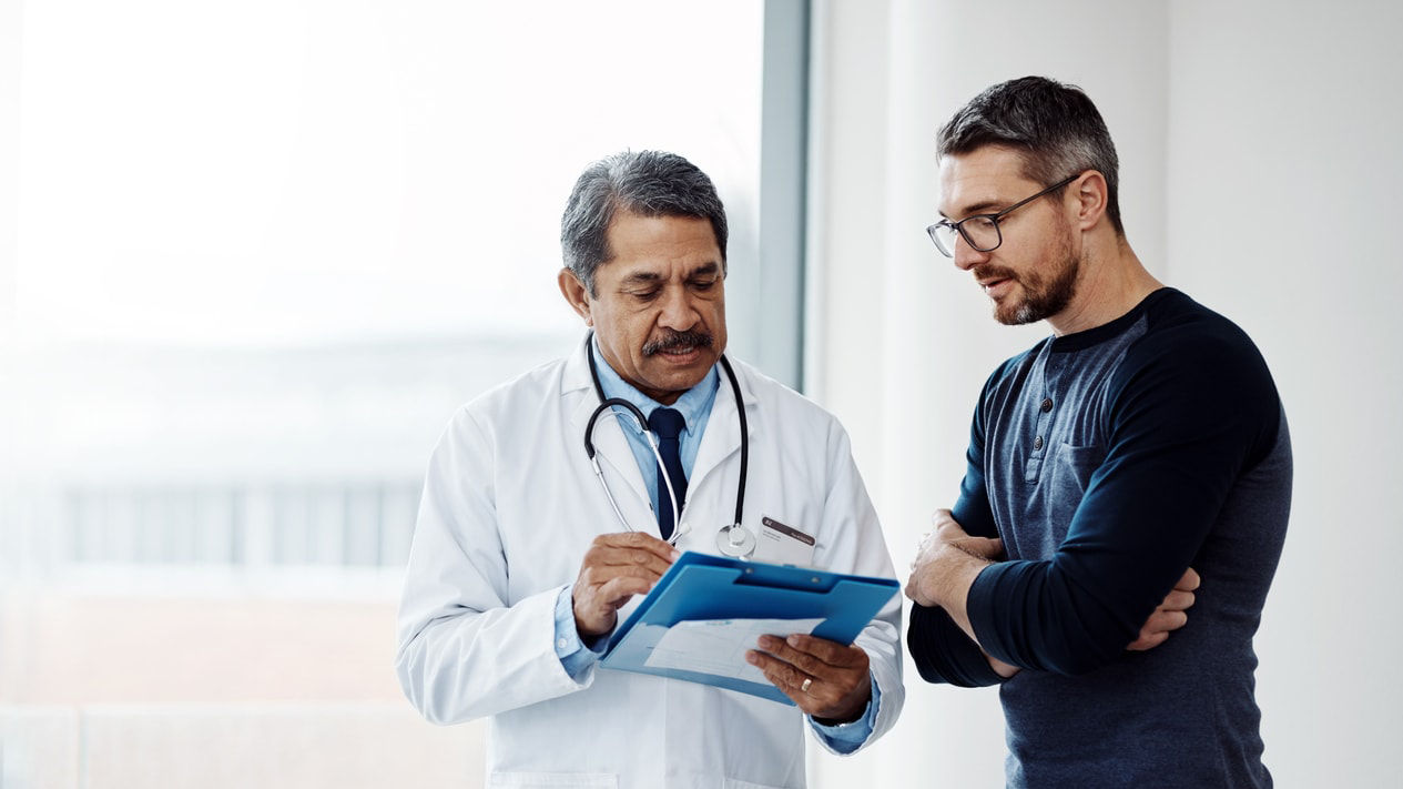 A male doctor is talking to a male patient in a doctor's office.