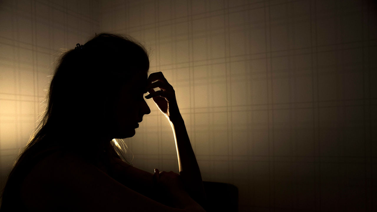 A woman is sitting in a dark room with her hand on her head.