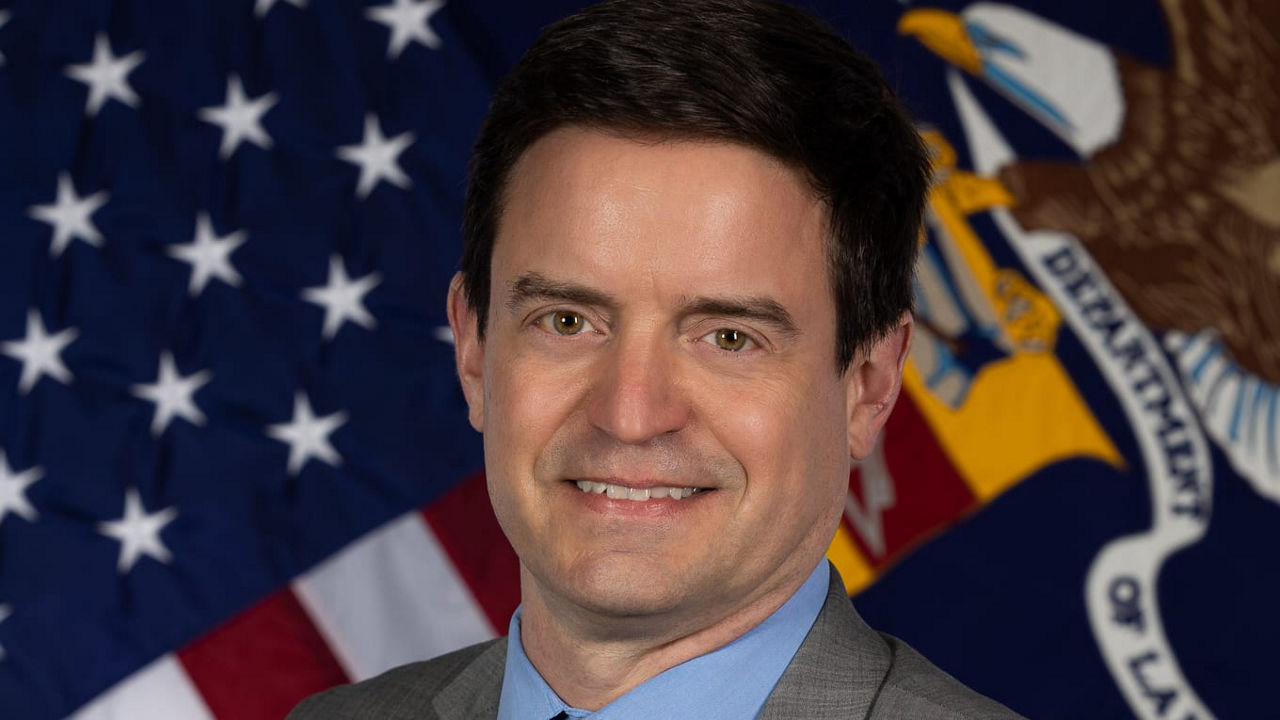A man in a suit and tie standing in front of an american flag.