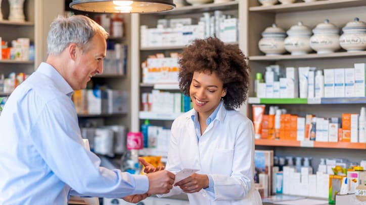 A pharmacist handing over a prescription to a customer in a pharmacy.