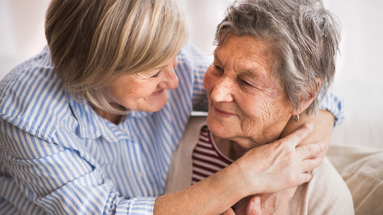 Two elderly women hugging each other on a couch.