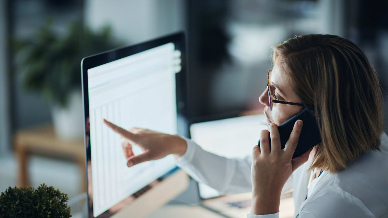 A woman talking on the phone in front of a computer screen.