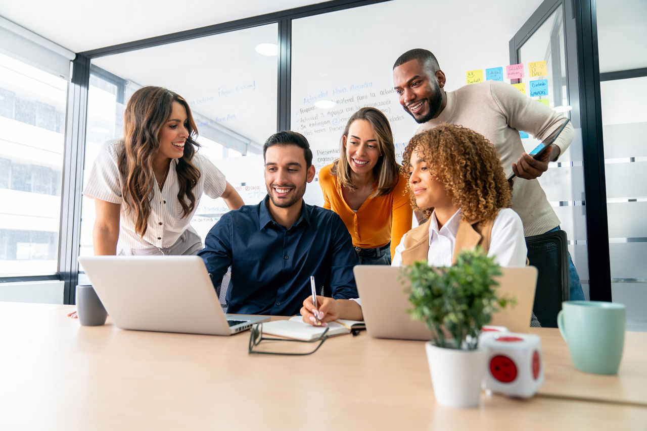 A happy group of coworkers sharing ideas in a business meeting and smiling while using a laptop