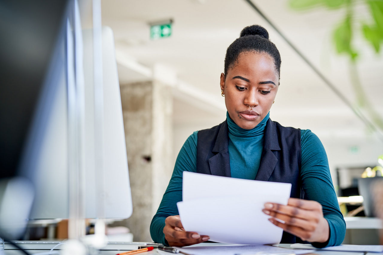 Businesswoman reviewing some documents sitting at her desk. Young female professional going through paperwork at coworking office.