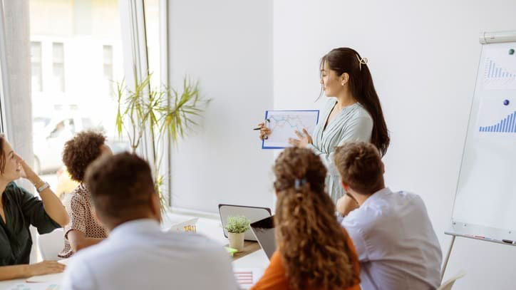 A woman giving a presentation to a group of people in a meeting room.