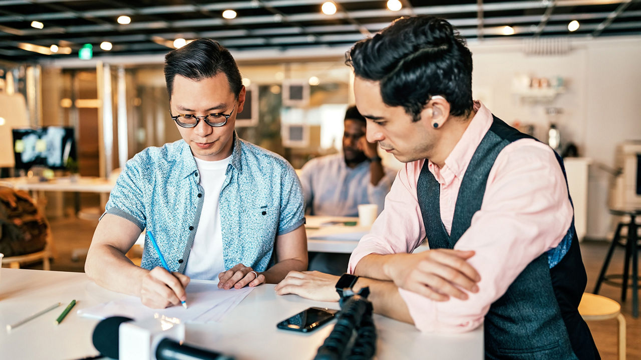 two people around a desk looking at person drawing something