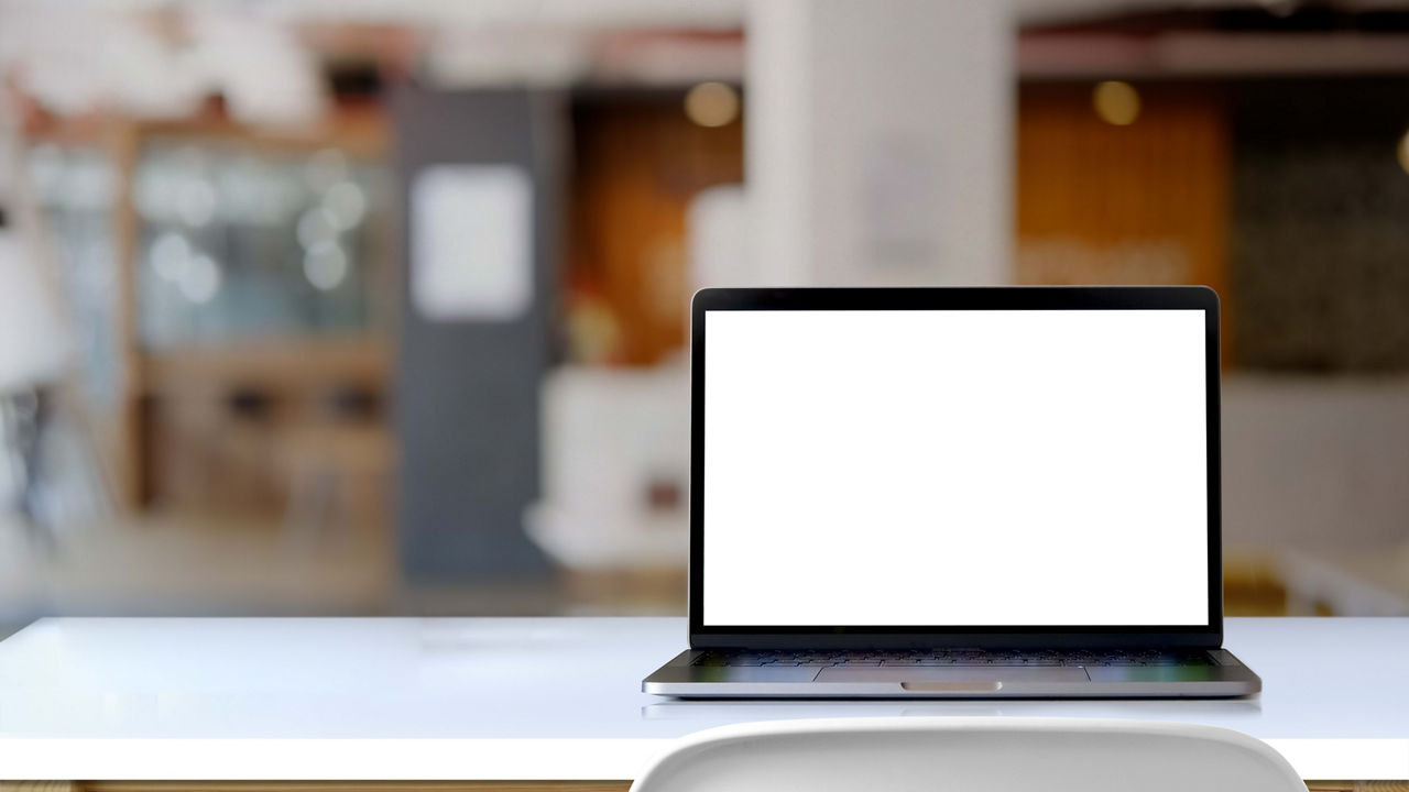 A laptop on a white table with a blank screen.