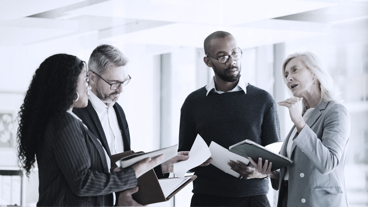 Four executives standing talking and holding papers