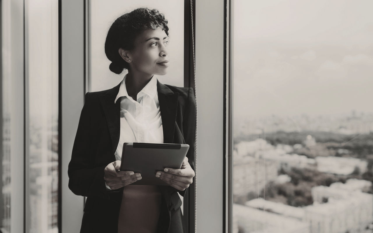 Female executive looking out window and holding a clipboard.
