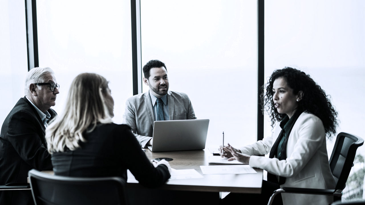 3 executives sitting around table listening to female executive on right talking
