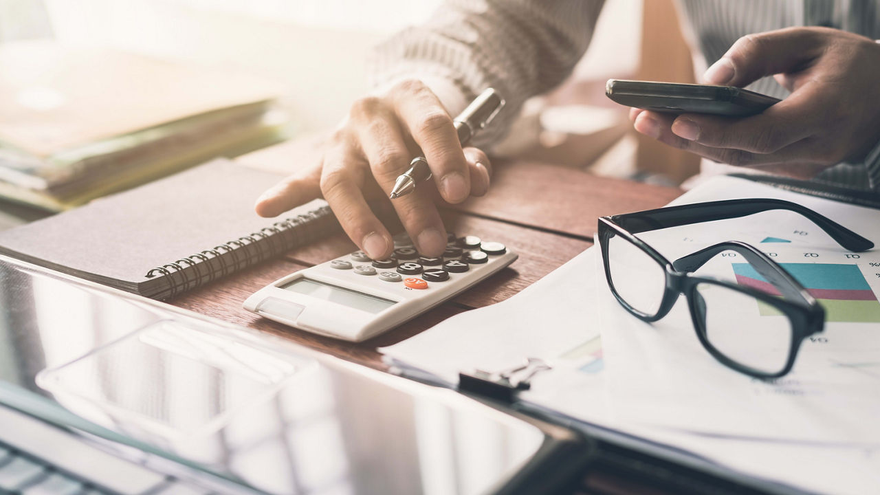 A man using a calculator and a cell phone at a desk.