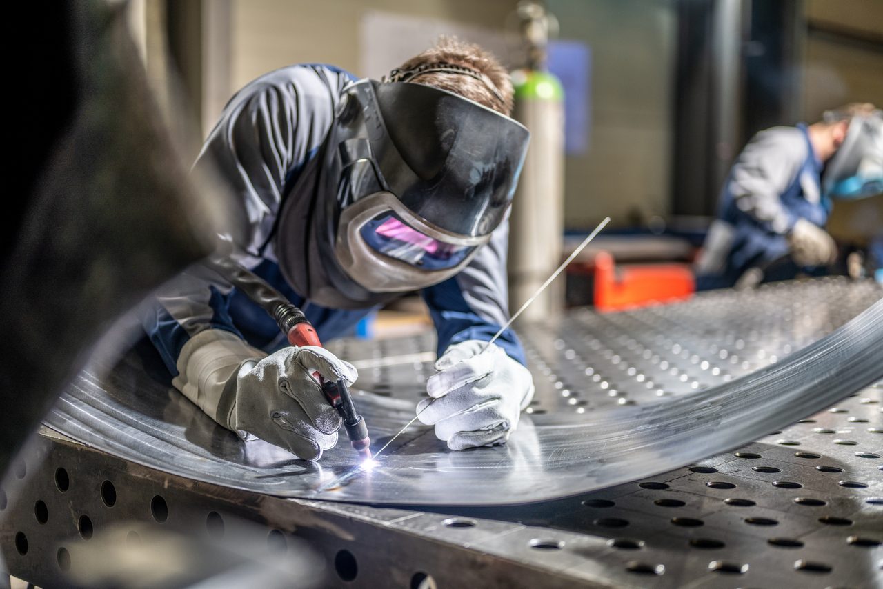 Male welder wearing helmet working with welding torch in factory.