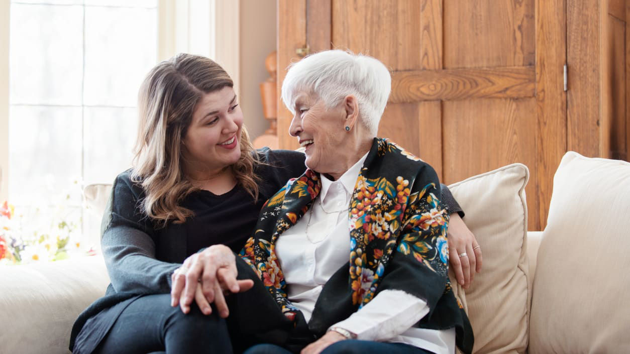 A woman is sitting on a couch with an older woman.