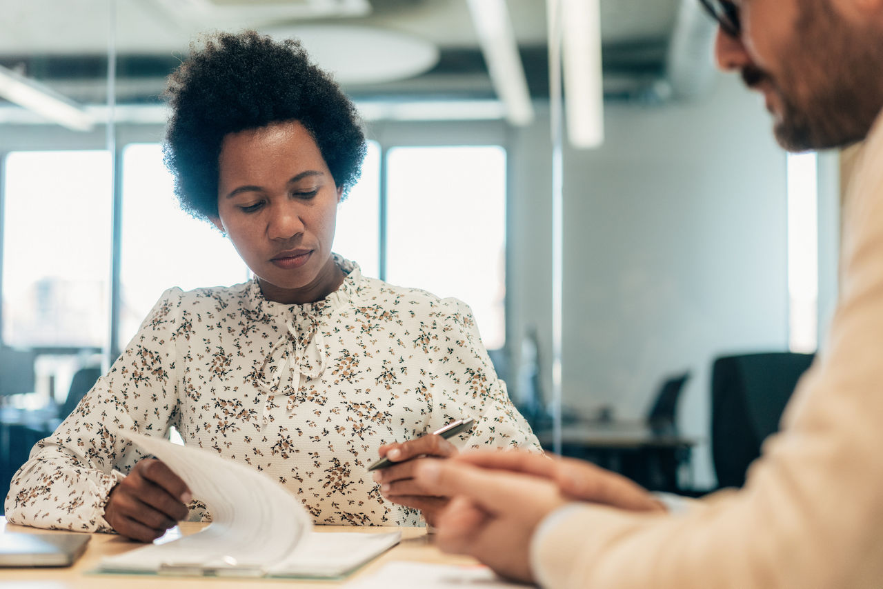 Business persons discussing new agreement. Business woman ready to sign contract at the office. Two business persons with formal paper. Business people signing a contract after successful agreement. Business persons filling in paperwork in an office. Multi ethnic business persons signing a document in board room.