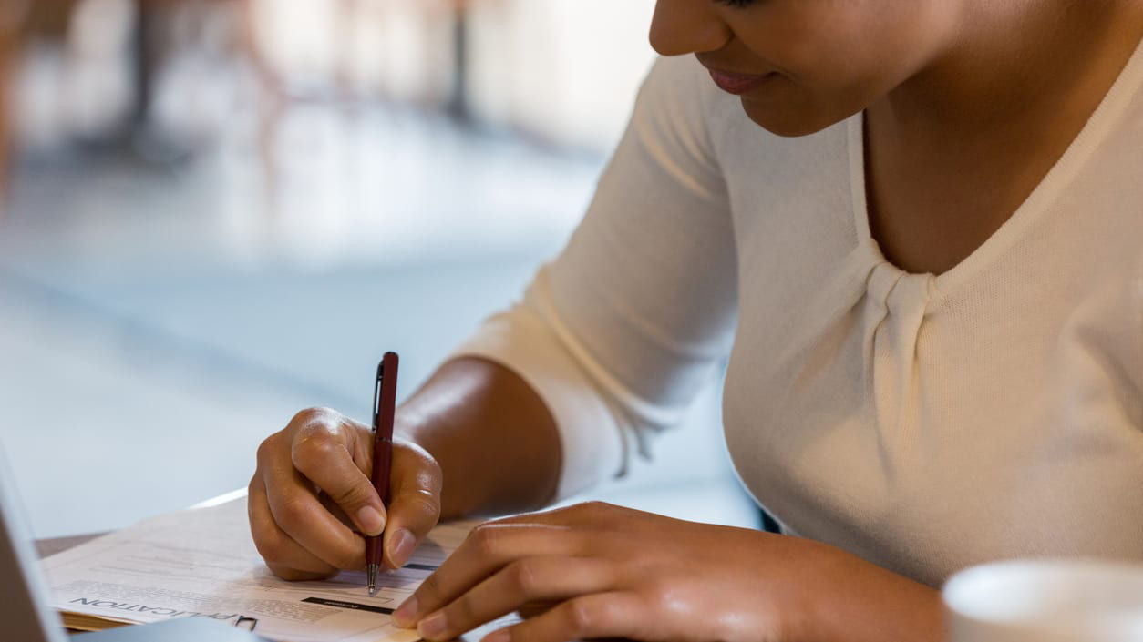 A woman writing on a laptop while sitting at a table.