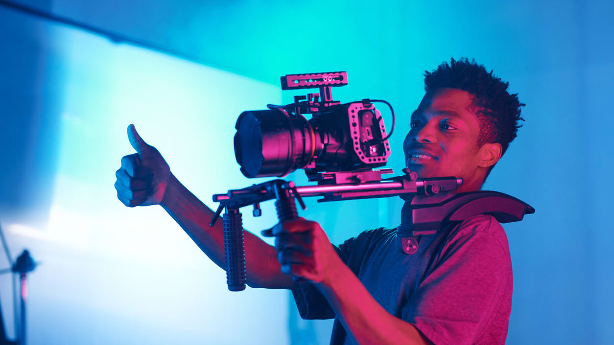 A young man holding a camera and giving a thumbs up.