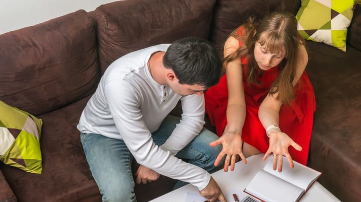 A man and woman sitting on a couch with a notebook and a calculator.