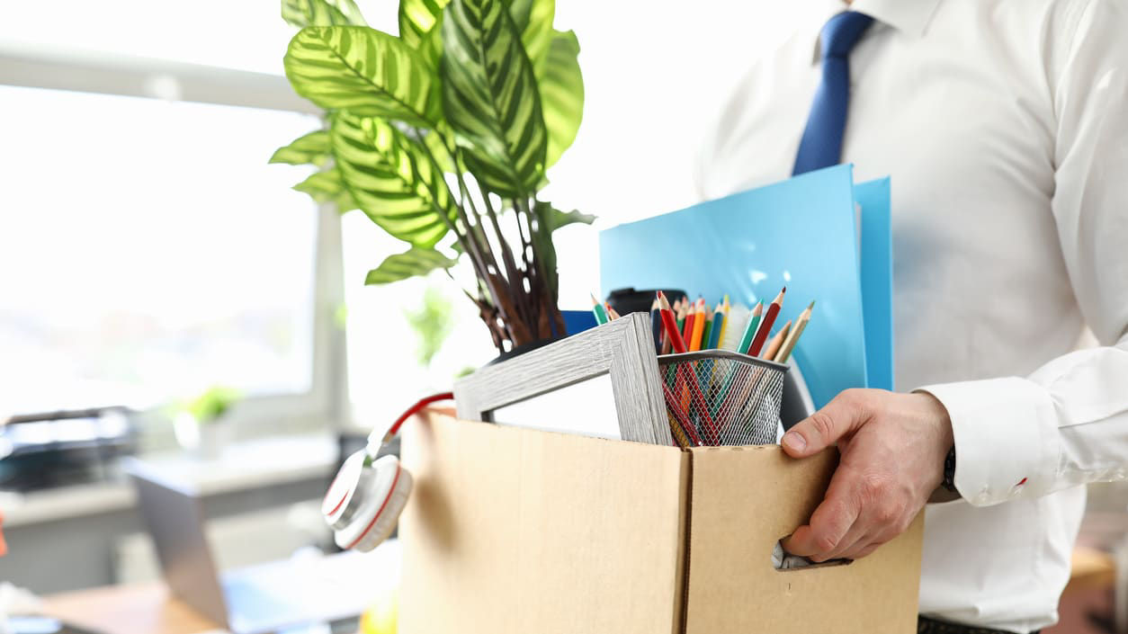 A man is holding a cardboard box full of office supplies.