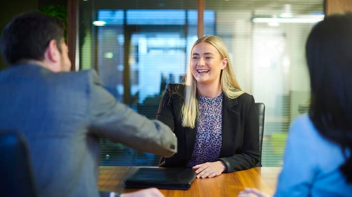 A business woman shaking hands with a man in an office.