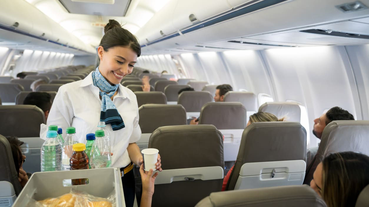A flight attendant is holding a tray of food in an airplane.