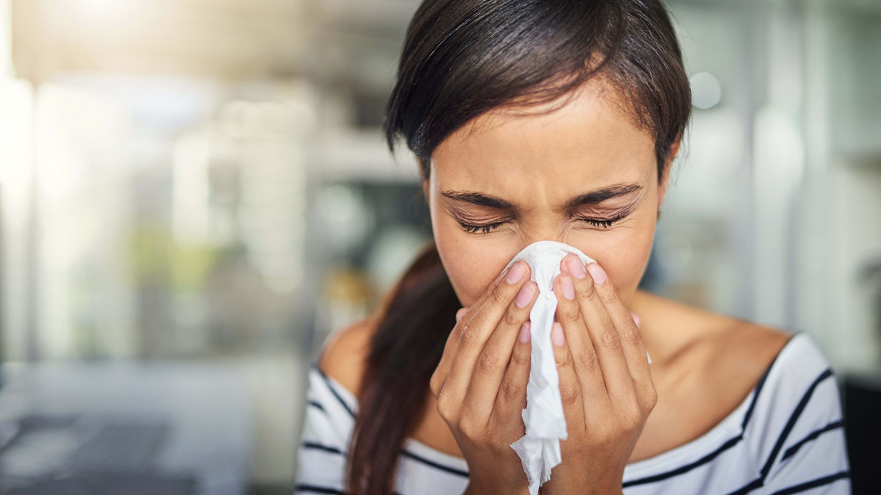 A woman blowing her nose with a tissue.