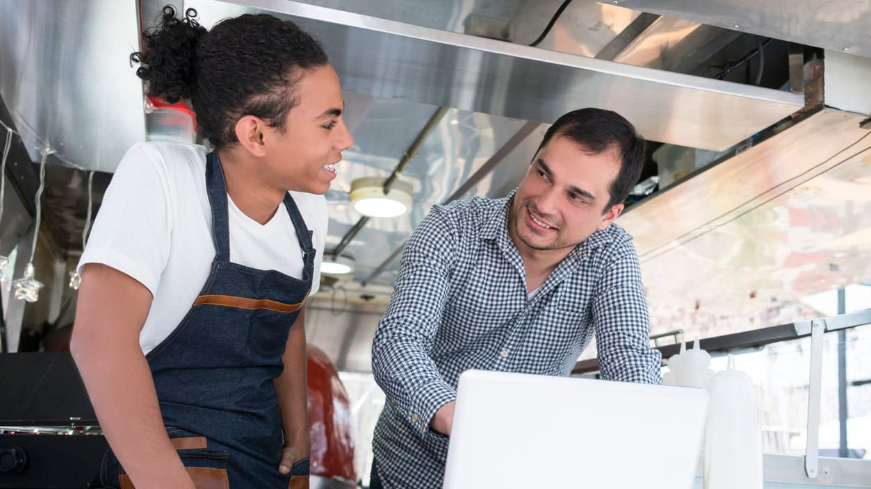 Two men working on a laptop in a food truck.