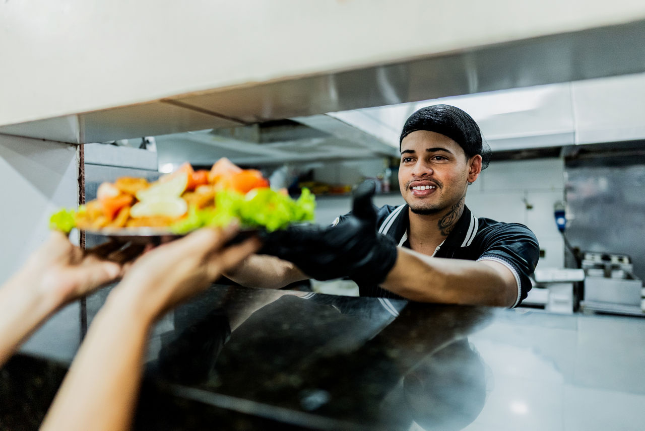 Young chef man passing platter with food to waiter at restaurant