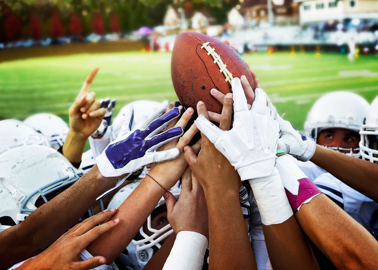 Football team members raising a football together in the air