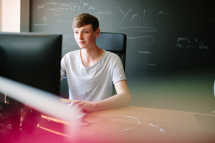 Indoor shot of a young man sitting at his desk in office and working on computer