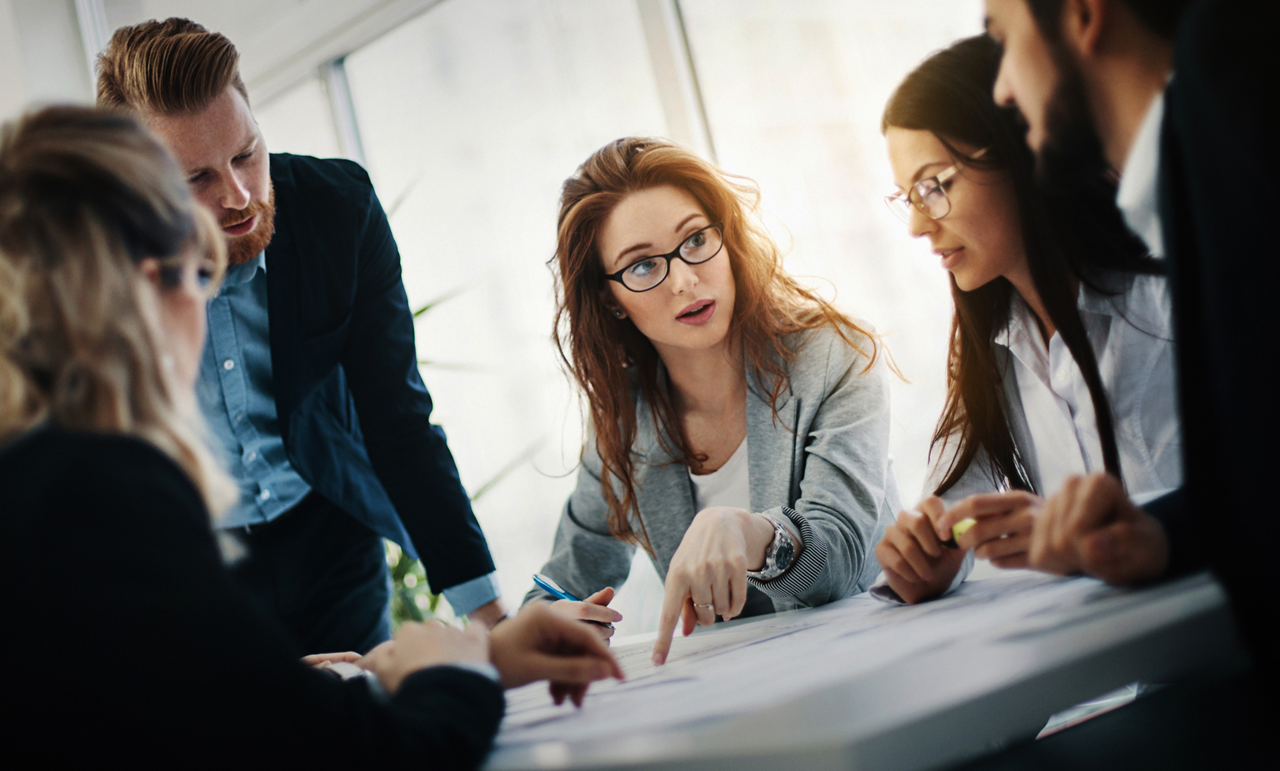 Closeup of mid 20's and early 30's entrepreneurs having a meeting considering their startup internet based company. There are three women and two men gathered around office desk and discussing their plans.