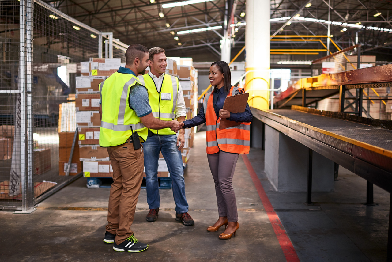 Shot of two workers shaking hands together while standing in a large warehouse