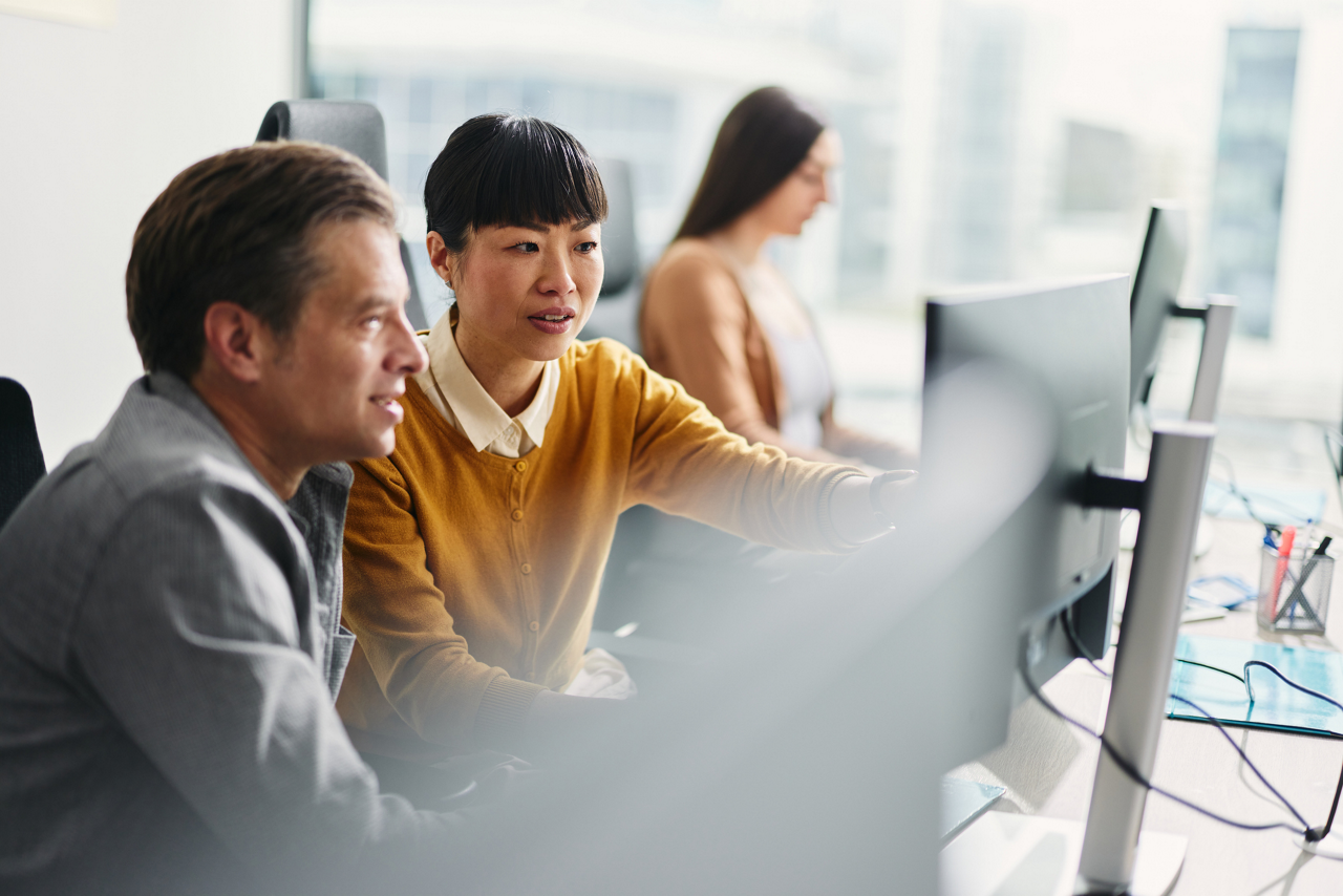 Business colleagues cooperating while reading codes on desktop PC at corporate office. Focus is on woman.