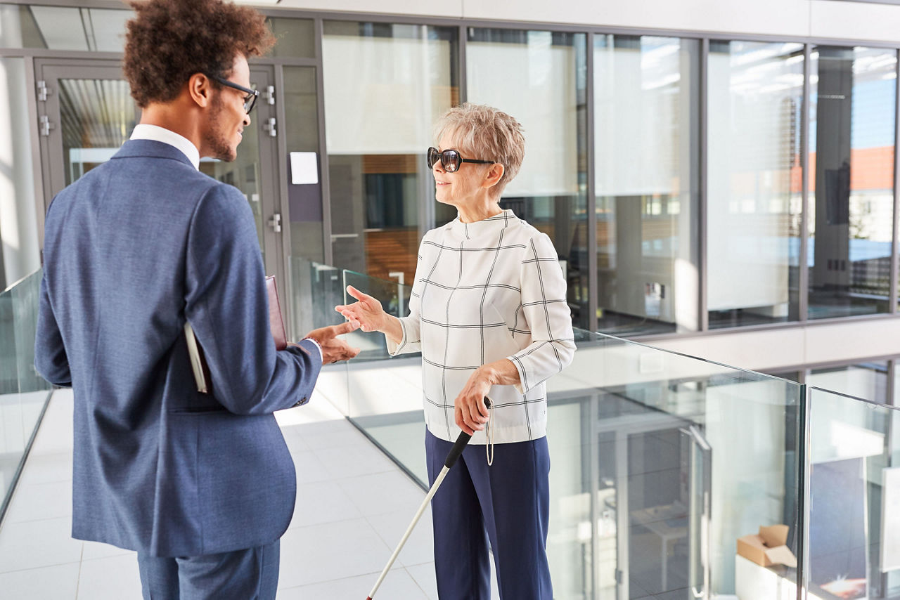 Blind businesswoman with long stick talking to African businessman