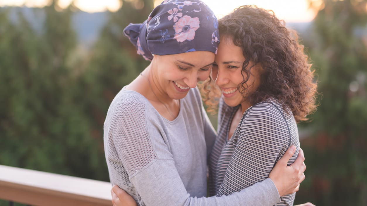 Two women hugging on a deck at sunset.