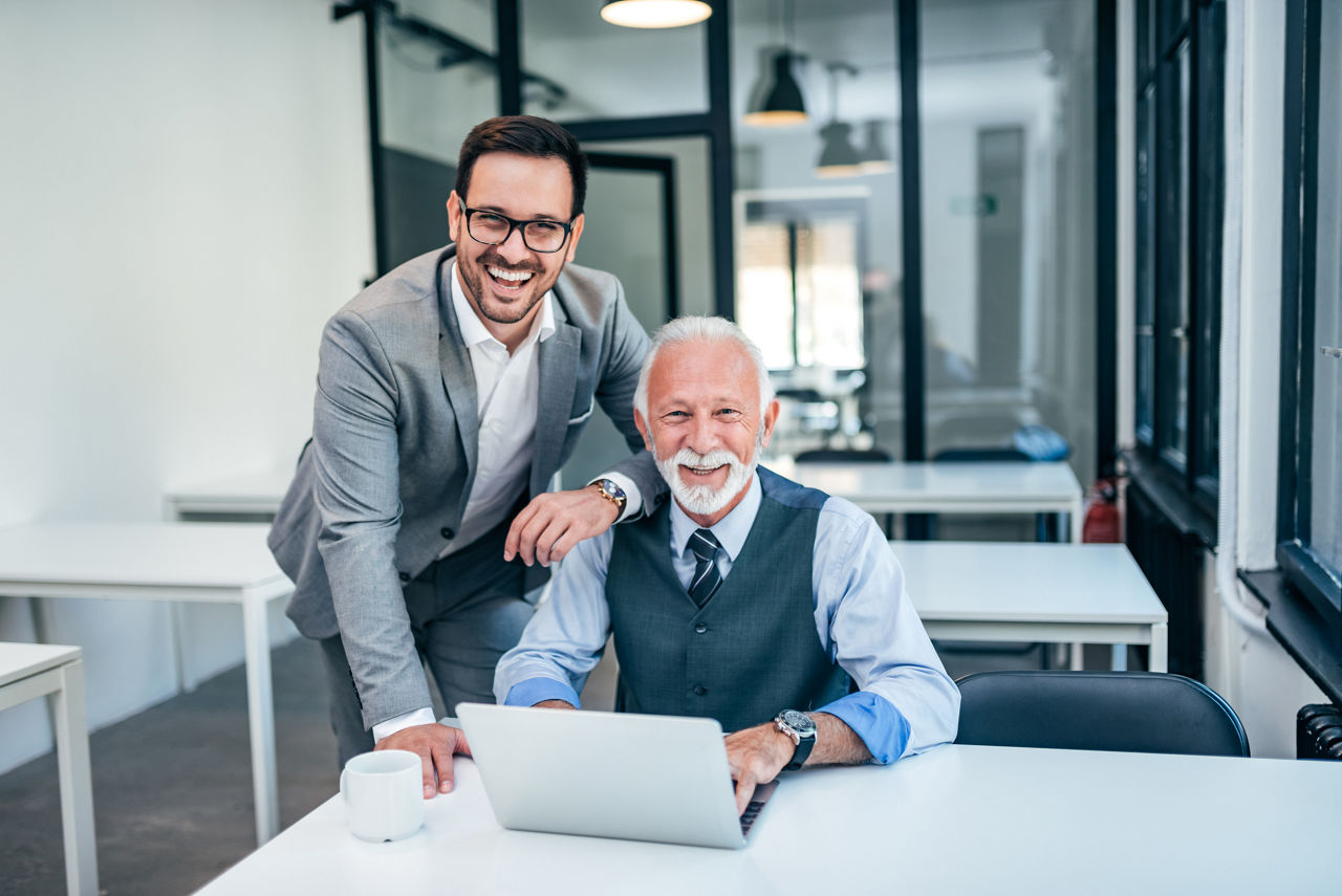 Older worker and younger worker smiling while working together.