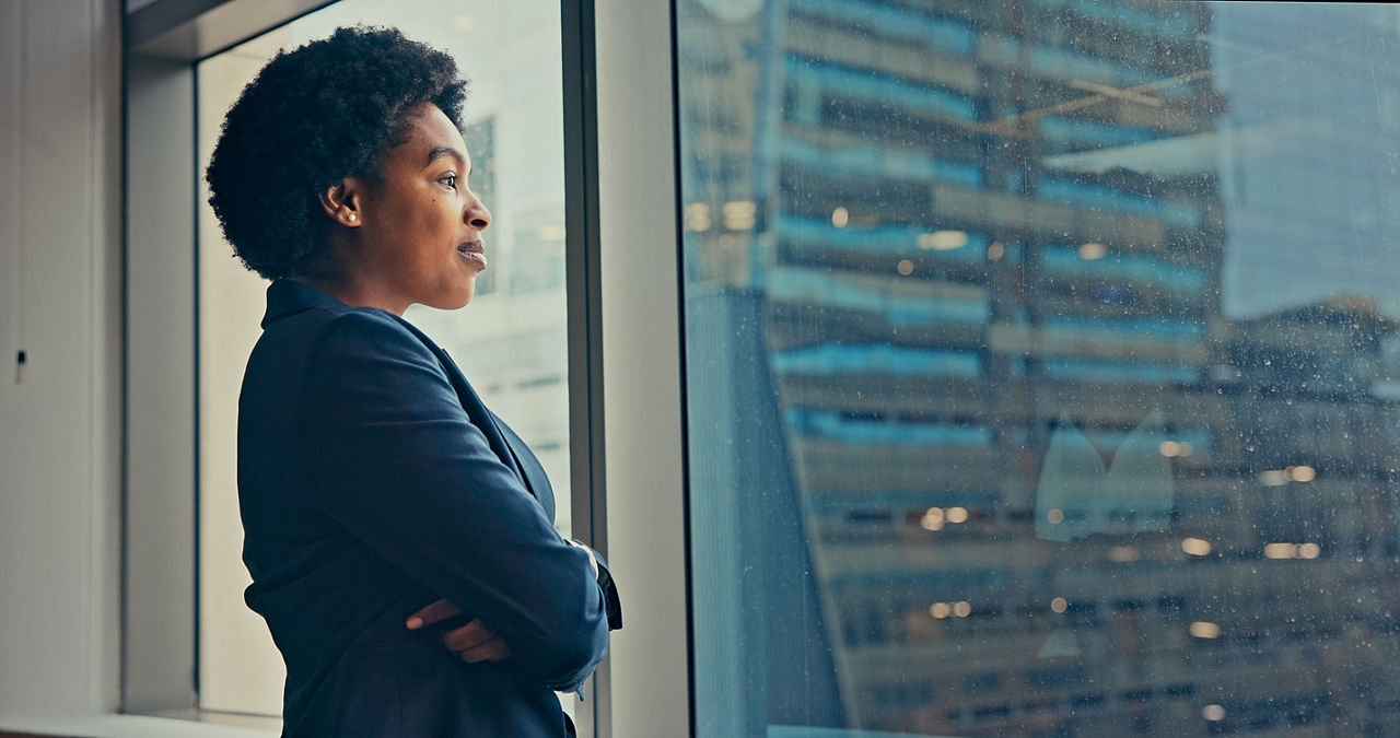 Successful Businesswoman Looking out of the Window at Big City in Downtown Area. Confident Female CEO Working on Financial Projects. Manager at Work Planning Marketing Campaign.