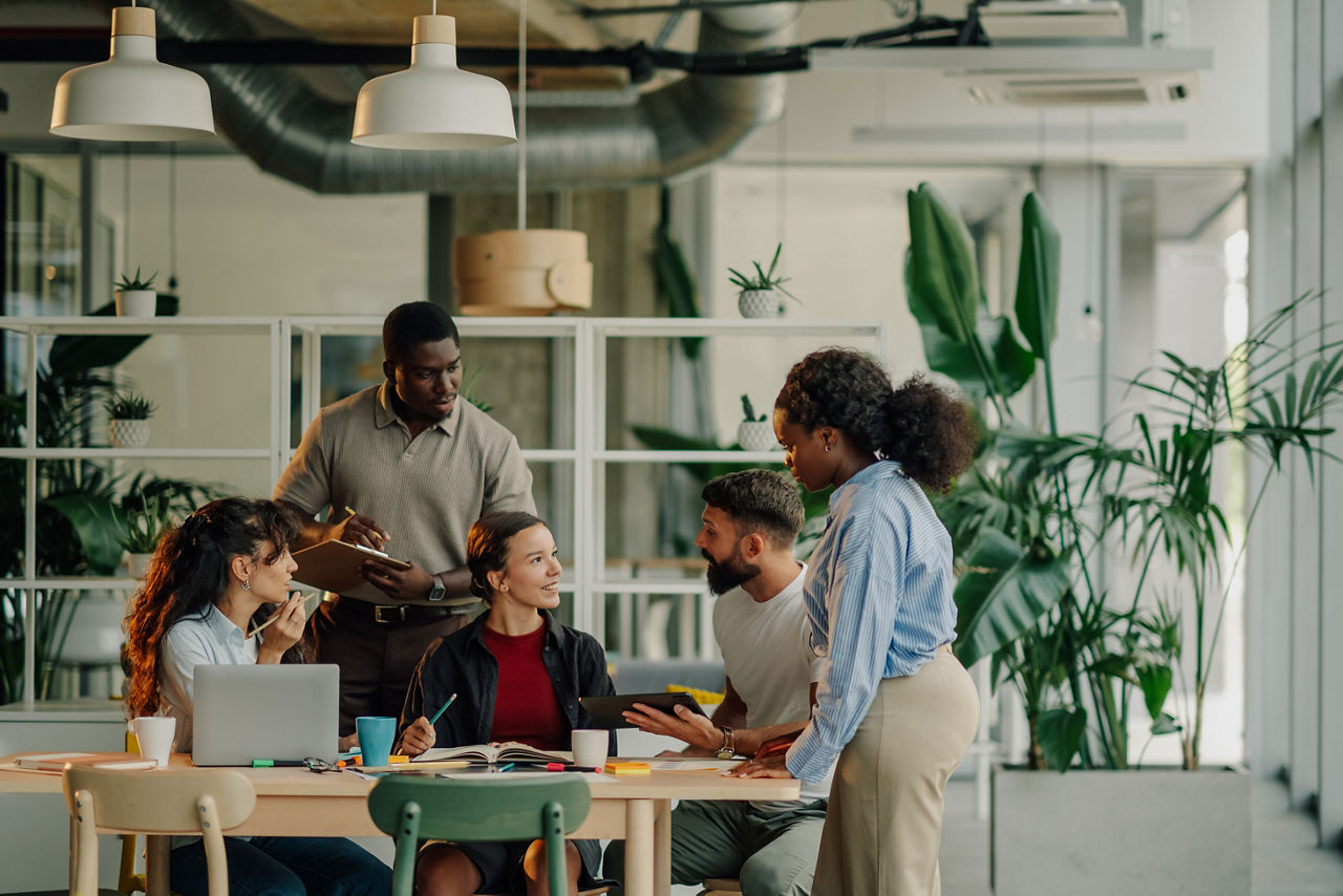 Group of young professionals working together, sharing ideas and using technology in a bright, plant-filled workspace