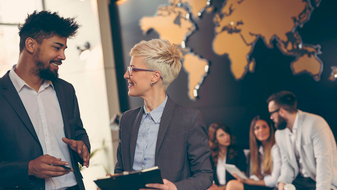 Two business people talking in front of a world map.