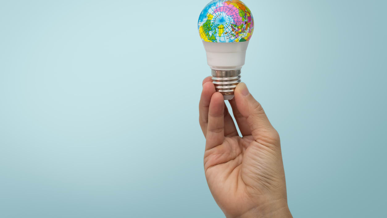 A woman's hand holding a colorful light bulb on a blue background.