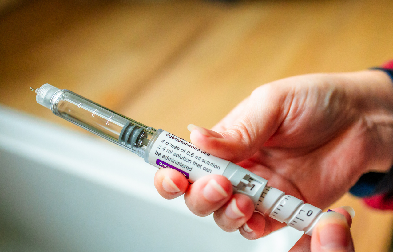 Close up of a woman's hands holding a weight loss injection pen. She is preparing to inject the dose into her abdomen.