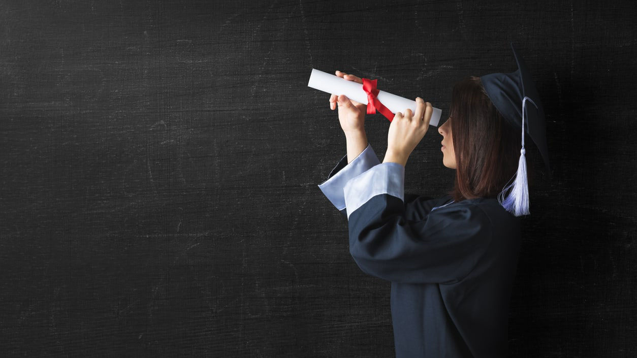 A woman in a graduation gown looking through a diploma.