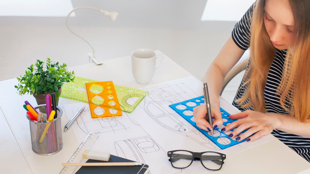A woman is working on a drawing at a desk.