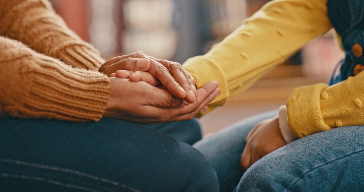 closeup of two people holding hands, symbolizing comfort or grief